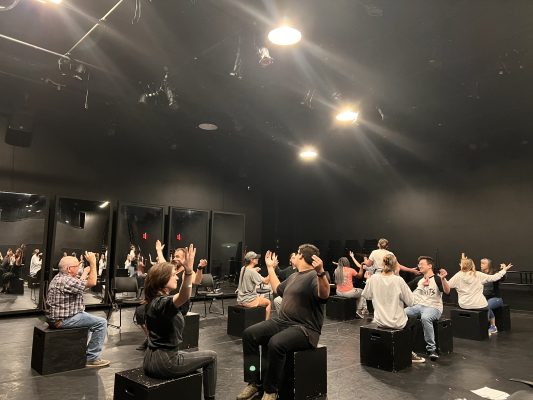 Actors on stage sitting on boxes during rehearsal