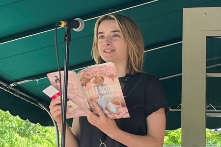 Isabella Anderson reading out of a book in front of a microphone on a stage