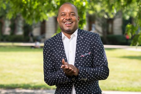 Jeffrey McCune stands on a campus in navy polka-dotted jacket and white shirt