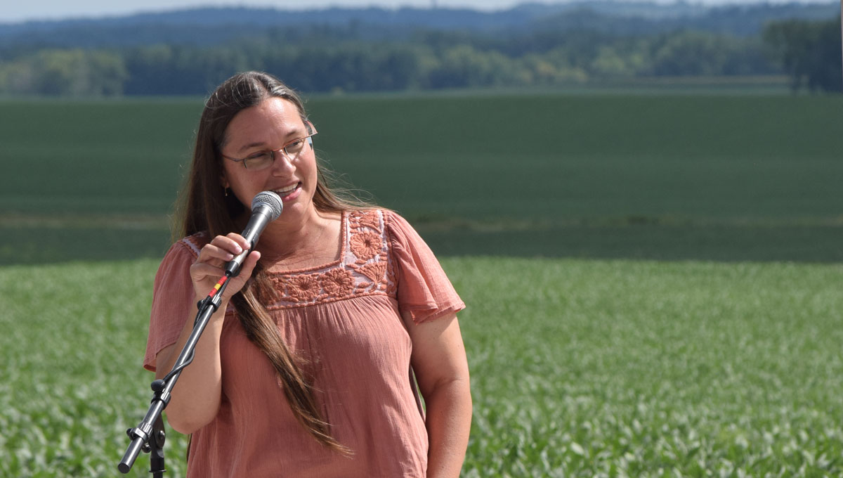 Jessica Wiskus with speaking into microphone with farm fields behind her