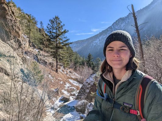 Mountain and snow scene behind student wearing a hat and winter coat