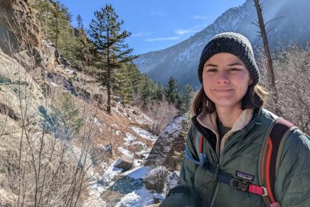 Mountain and snow scene behind student wearing a hat and winter coat