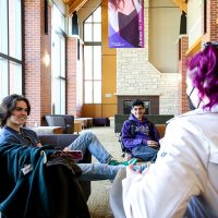 Three students chat in the chairs in Thomas Commons lobby