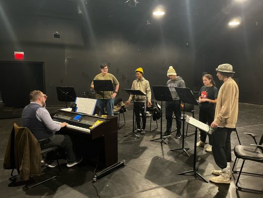 Five students standing in front of a pianist with music stands during rehearsal