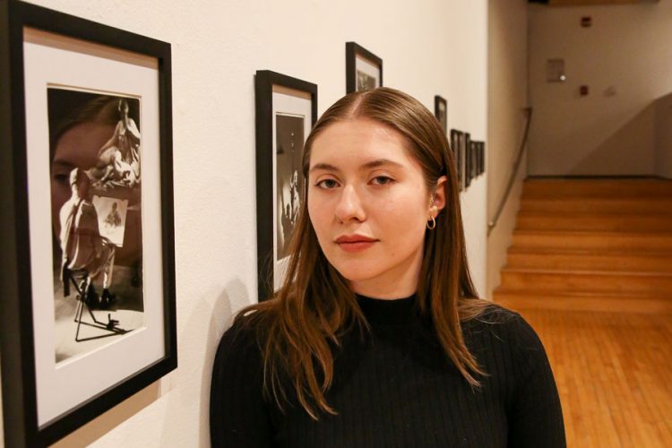 Emma Titus ՚23 stands beside her senior art exhibit at the Peter Paul Luce Gallery in McWethy Hall. Her show, “Alterations & Repairs,” featured photos shot on the streets of New York. Photo by Megan Amr.