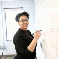 melanie king holding a whiteboard marker in front of a whiteboard smiling