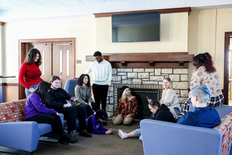 Now: 11 students recreated the historical photo inside Pfeiffer Hall lounge with some 2023 energy. Standing from left: Marley Gillespie ’26 and Michael-Sean Ossai ’26. Seated from left: Kaylanna Seu ’25, Parker Townsend ’23, Olivia Cotton ’26, Lillian Leon ’25 (on the floor), Natalie Zenk ’25, Amelia Anderson ’25 (on the floor), Amina-arwa Abdullahi ’26 (on the arm of the chair), and Wybie Warmbold ’26. Reclining on the floor: Adrien Kaplan-Mazur ’25.