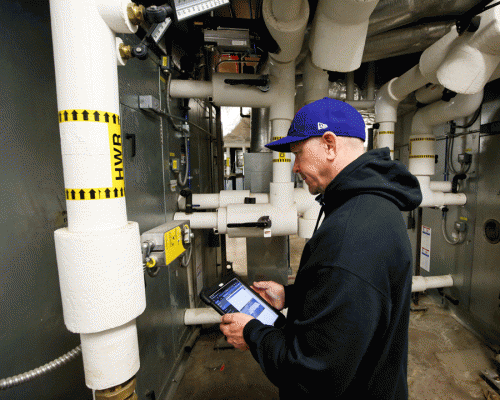 Thomas Thomas is pictured inside the Thomas Commons top level where he is using an iPad to check on operations of an air handler and hot water lines