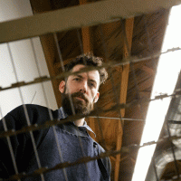 alex mckenzie standing behind a mesh net, a wooden ceiling is the backdrop