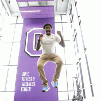 Lewis Kanyiba jumping in the air in front of a purple background with large windows letting sunlight in