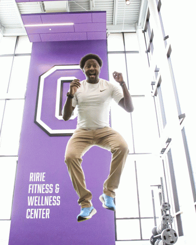 Lewis Kanyiba is jumping, he is completely in the air. The background is a purple sign and the cornell C