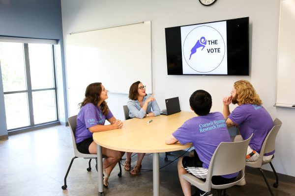 Three students and Professor Goldberg look up at a screen with a sticker design and the word "Ram the Vote."