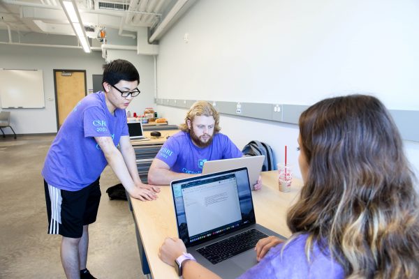 Three students sit at a table with laptops