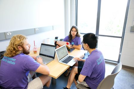 Three students sit together at a table with labtops.