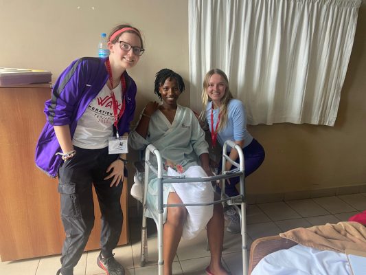 Sam and Elinor sitting by a woman who has a walker in front of her.