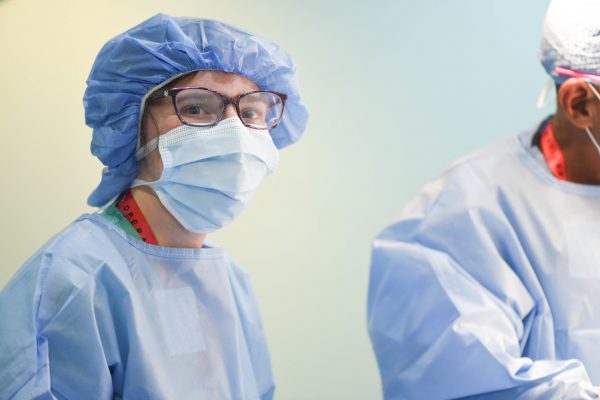 Elinor looking at the camera wearing all blue scrubs, including a face mask.