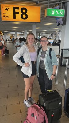 Two students stand with their suitcases in an airport.