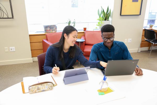 Photo of Caitlyne sitting next to a student pointing to his computer.