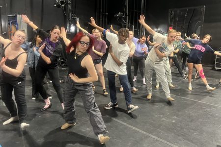 Several students dancing with their arms in the air and one leg kicked out.