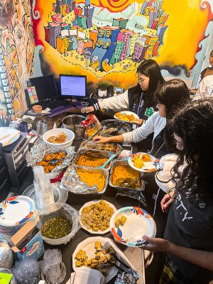 Three students filling their plate and a table filled with a variety of foods.