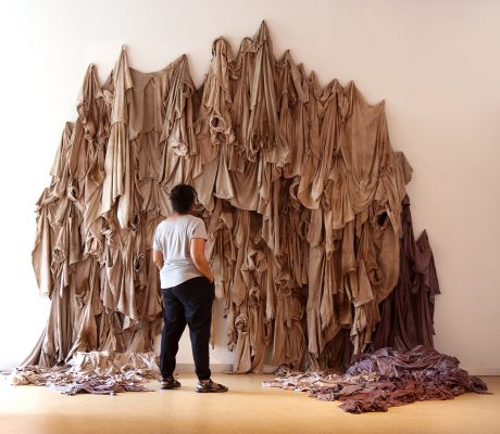 Person standing in front of a large, brown textile art piece.