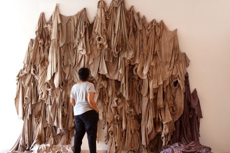 Person standing in front of a large, brown textile art piece.