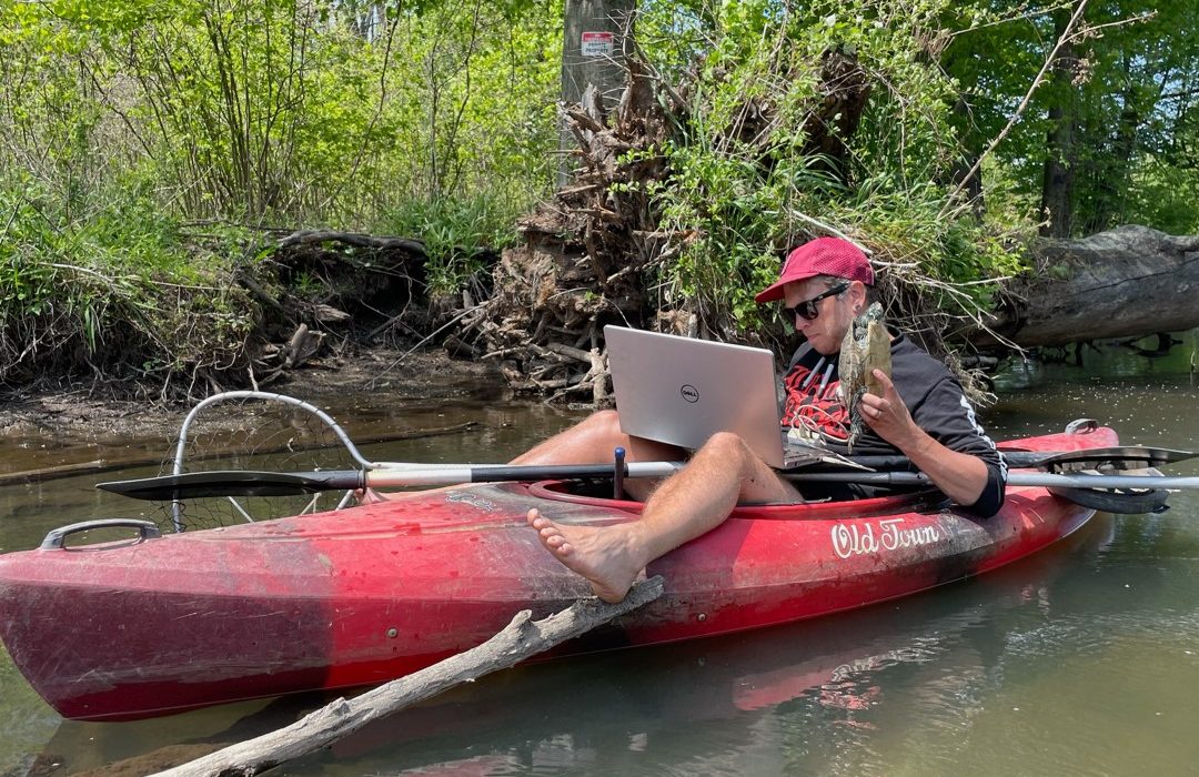 Joshua Otten sitting in a kayak with a computer, while holding a turtle. Photo courtesy Josh Otten.