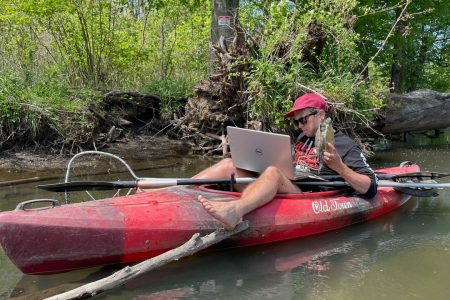 Joshua Otten sitting in a kayak with a computer, while holding a turtle. Photo courtesy Josh Otten.