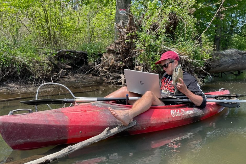 Joshua Otten sitting in a kayak with a computer, while holding a turtle. Photo courtesy Josh Otten.