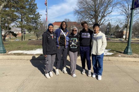 Five students standing outside in front of a college campus