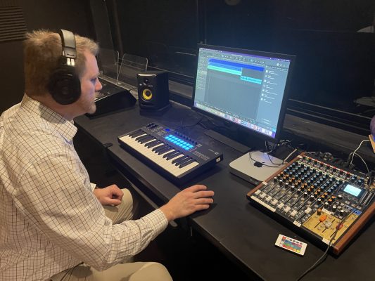 Professor sits at a computer  with headphones on.