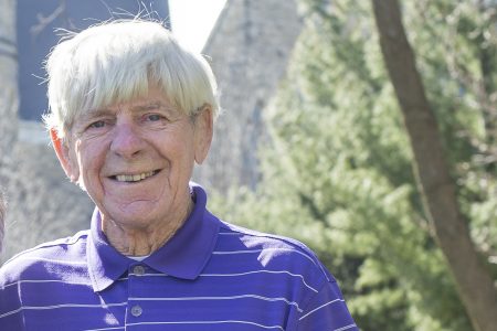 Robert Majors ’57 in purple and white striped polo shirt standing outdoors