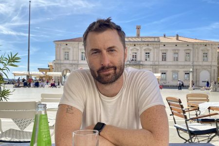 Dustin Waite ’06 sits at a table outdoors with a drink.