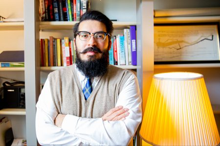 Jonathon Dreeze has taught history at Cornell since 2020. He stands, arms crossed, in his book-lined office.