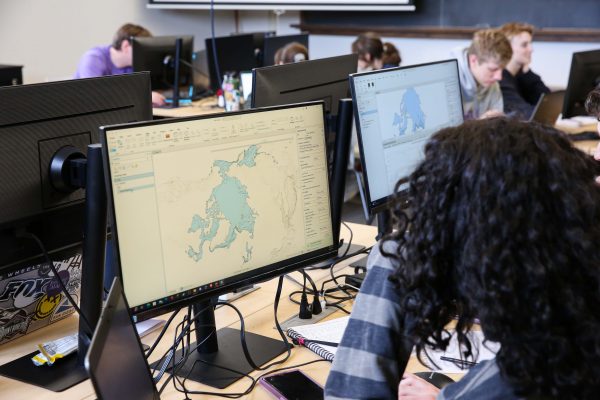 Students work on computers. Blue maps are seen in the monitors.