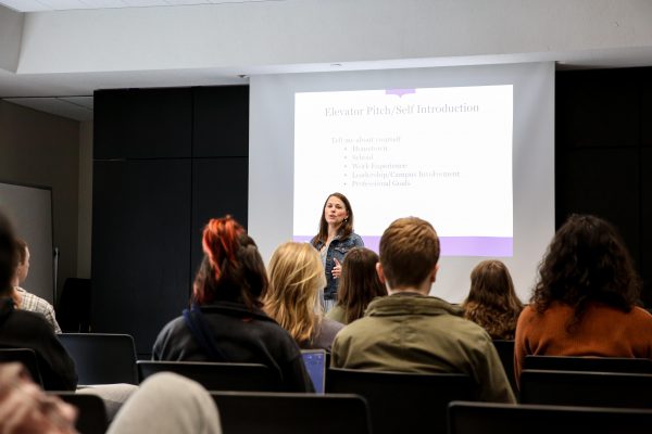 Jodi stands in front of a room with a presentation on the projector behind her. You can see the backs of several students.