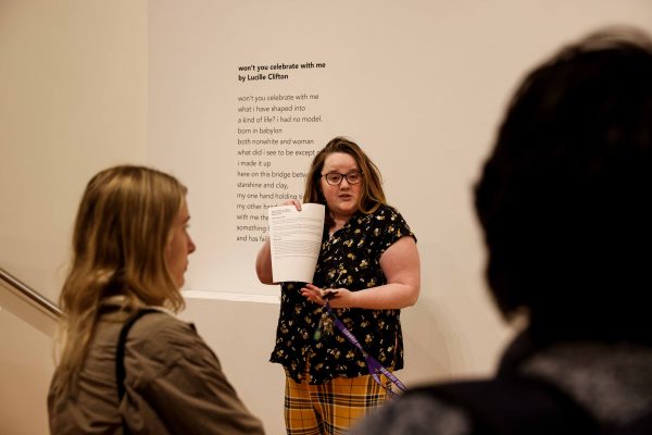 An instructor holding up a piece of paper with two students watching in the foreground.