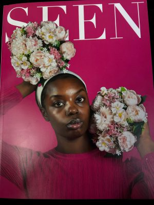 Photo of a woman of color holding flowers with a pink background and the title of a magazine "SEEN"