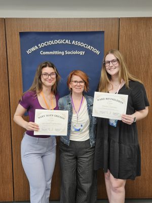 Two students and a professor stand for a photo while holding the awards for their research.