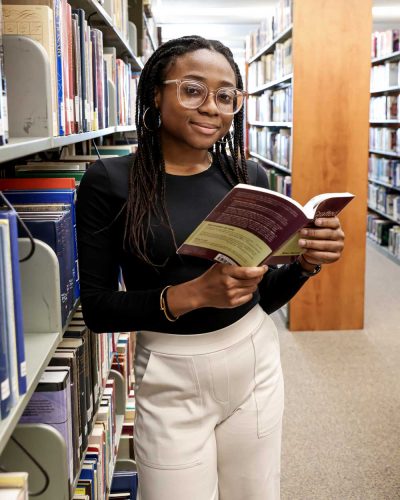 Kimberly Maitland '24 peers over a book in the stacks at Cole Library. 