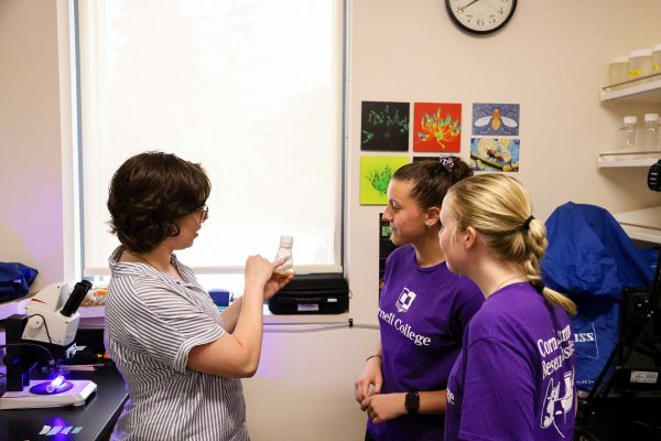 Two students look at a test tube of flies as the professor describes what's inside. 