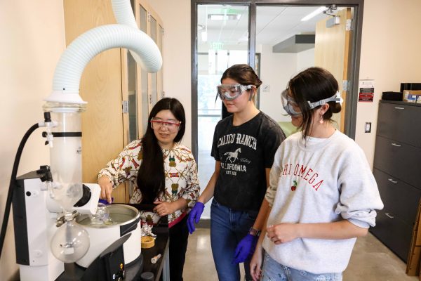 Two students and their professor work on an evaporator machine in a science lab.