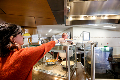 A student reaches forward to get a plate full of food from a cafe worker