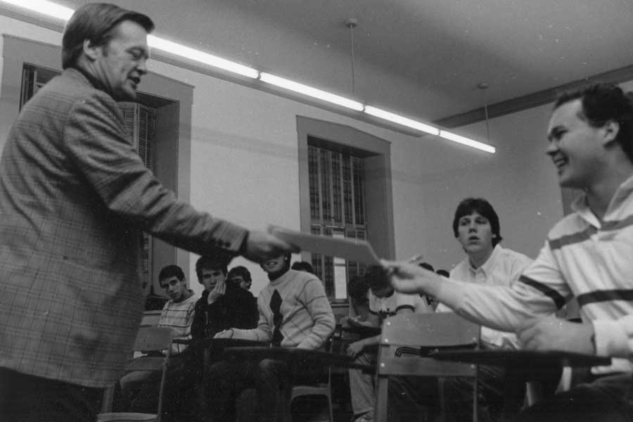 Professor Emeritus Gordon Urquhart hands a paper to a student in class.