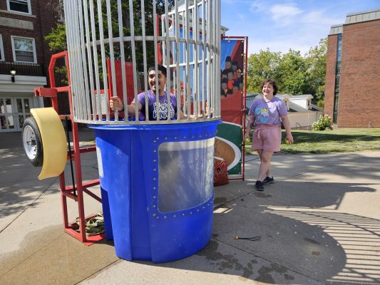 Student smiles at the camera while standing in the water of a dunk tank.