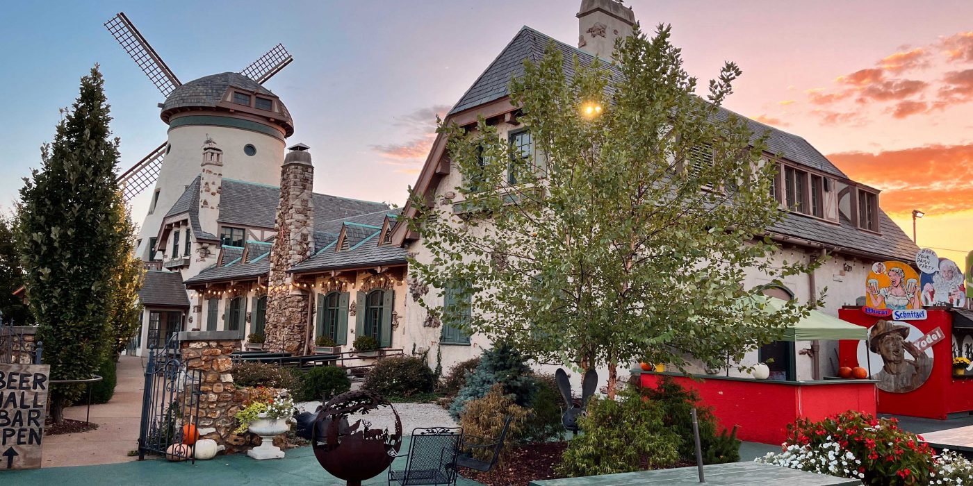 A German-style building with a windmill and the sunsetting in the background.