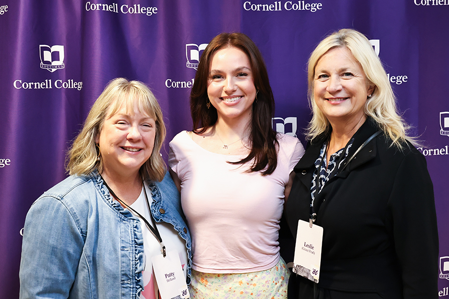 Patty Helland '86, Maggie Helland '26, and Leslie Grau Frady '86 pose in front of a Cornell step and repeat sign.