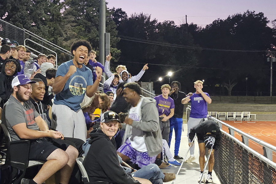 Students cheer from the football stands at dusk.