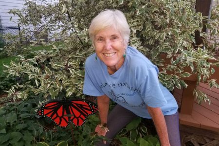 Sarah Binder '77 in T-shirt in a garden with a big butterfly decoration